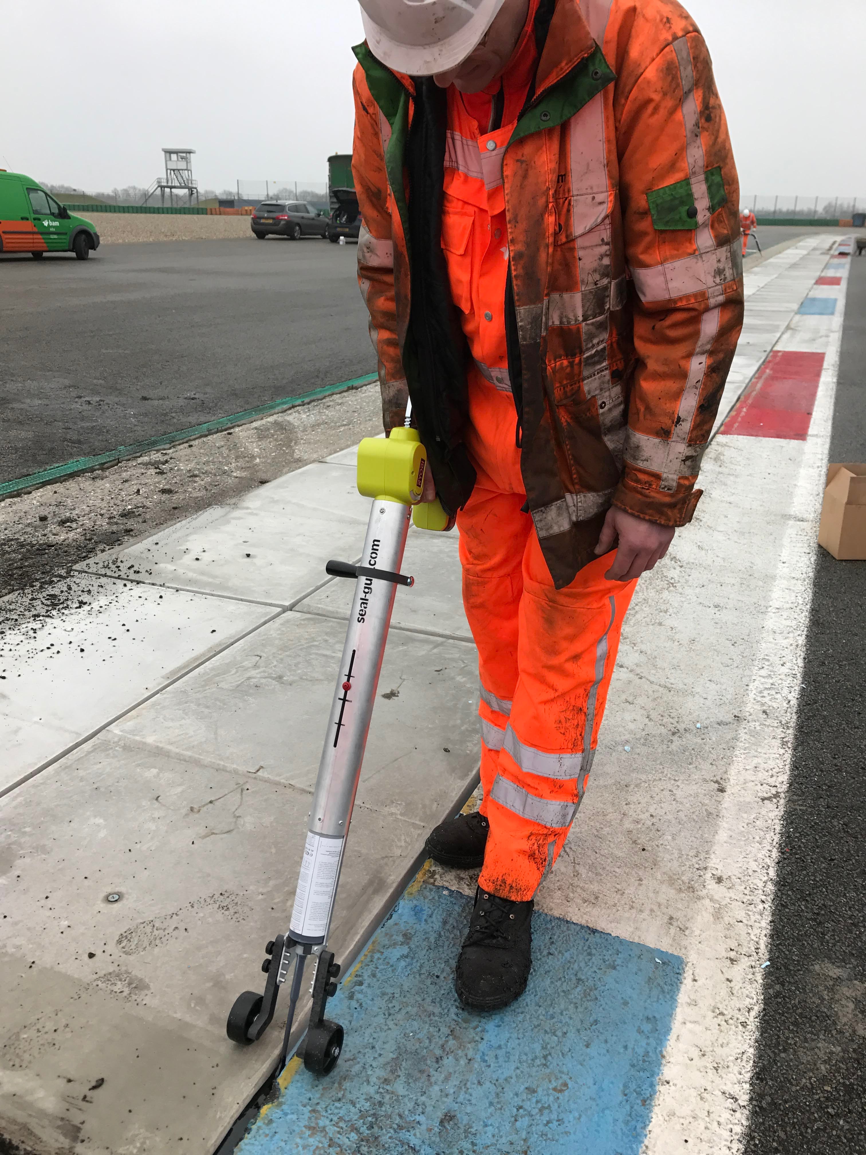 Werknemer in oranje werkkleding voert een meting uit langs de rand van een asfaltweg.